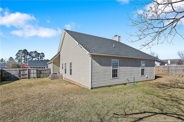 back of house featuring a fenced backyard, a chimney, a shingled roof, and a yard