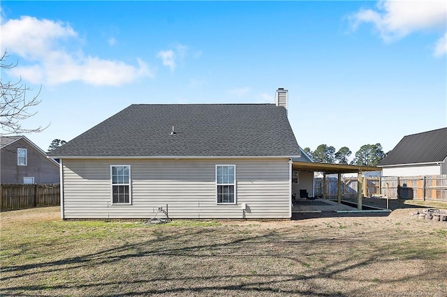 back of property with roof with shingles, a patio, a chimney, a lawn, and a fenced backyard