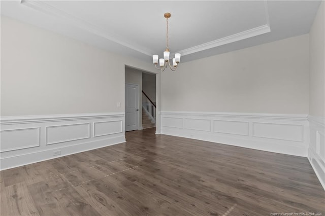 empty room with a raised ceiling, stairway, wood finished floors, crown molding, and a notable chandelier