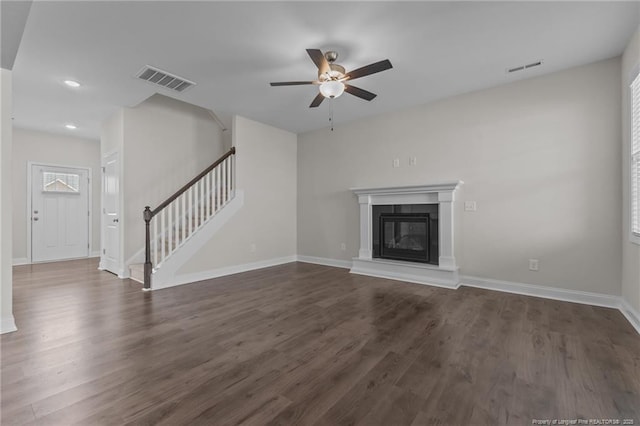 unfurnished living room with dark wood-style floors, a glass covered fireplace, visible vents, and stairway