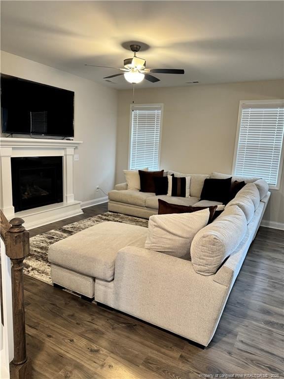 living room featuring ceiling fan, baseboards, a fireplace with raised hearth, and wood finished floors