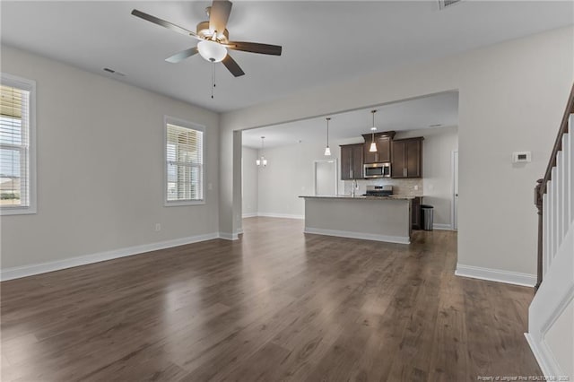 unfurnished living room with visible vents, baseboards, a ceiling fan, stairway, and dark wood finished floors