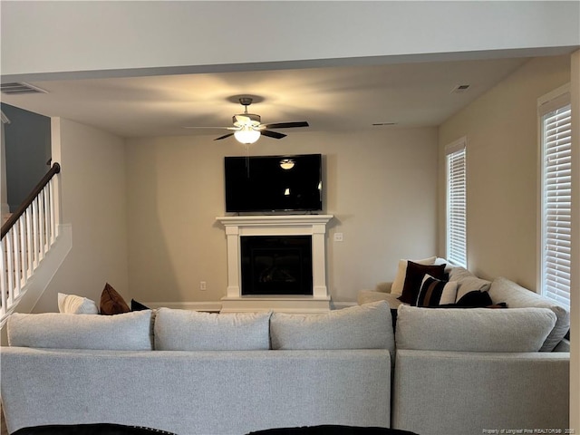 living room with a glass covered fireplace, visible vents, and ceiling fan