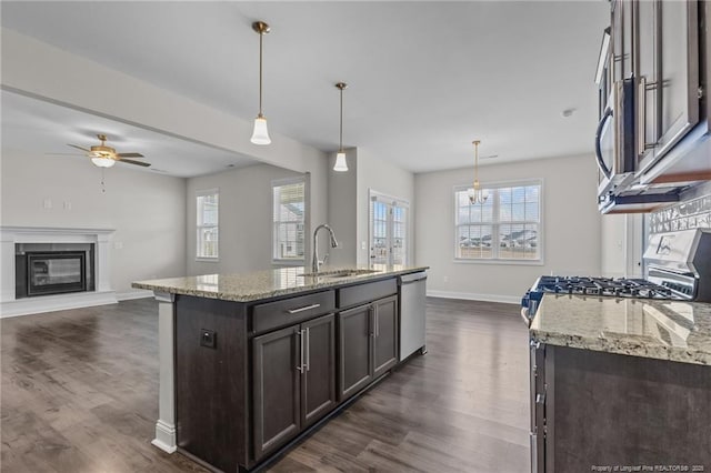 kitchen featuring dark brown cabinetry, a glass covered fireplace, dark wood-style floors, stainless steel appliances, and a sink