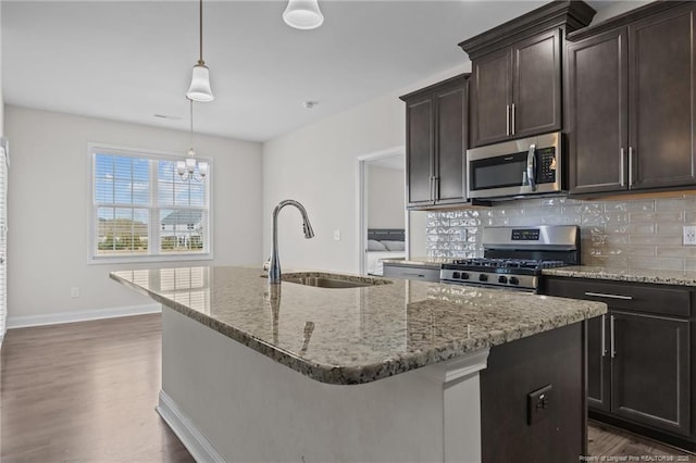 kitchen with tasteful backsplash, appliances with stainless steel finishes, light stone counters, a kitchen island with sink, and a sink