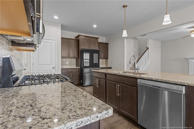 kitchen with tasteful backsplash, decorative light fixtures, light stone countertops, stainless steel appliances, and a sink