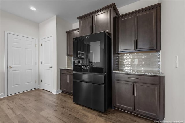 kitchen featuring dark brown cabinetry, dark wood-type flooring, freestanding refrigerator, light stone countertops, and backsplash