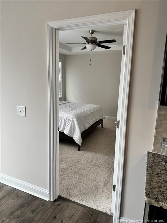 bedroom featuring a ceiling fan, baseboards, a raised ceiling, and dark wood-type flooring