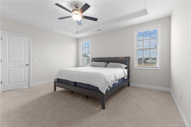 bedroom featuring a raised ceiling, light carpet, ceiling fan, and baseboards