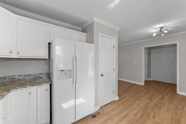 kitchen with ornamental molding, white refrigerator with ice dispenser, visible vents, and white cabinets