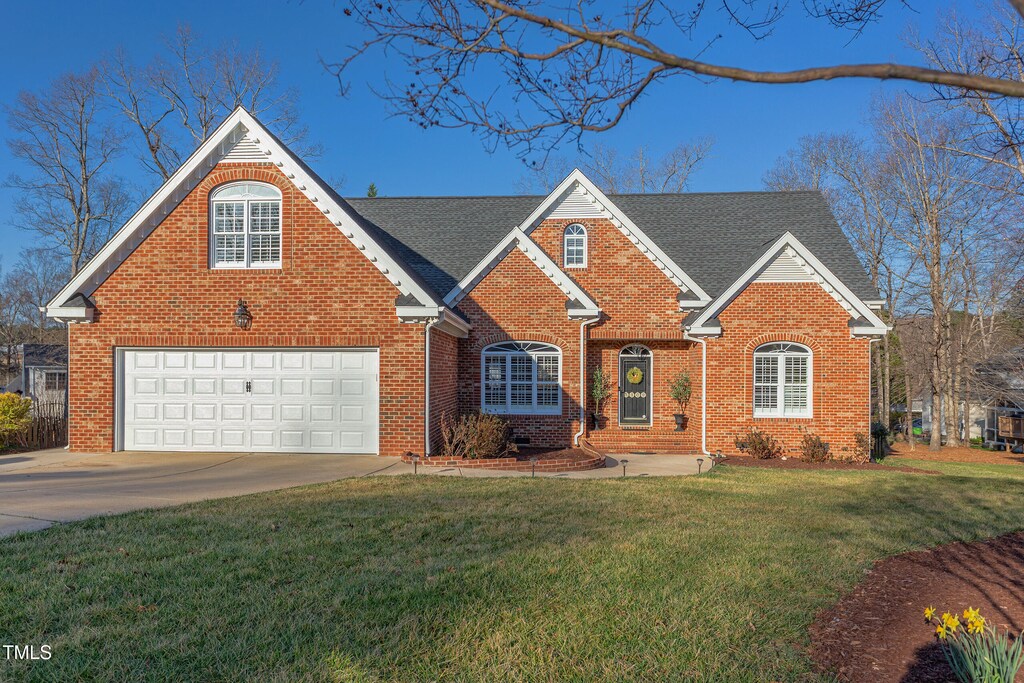 traditional-style home featuring brick siding, driveway, a shingled roof, and a front yard