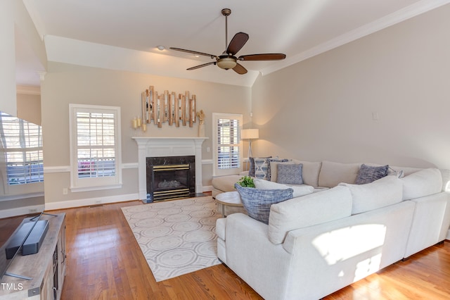 living area featuring crown molding, baseboards, ceiling fan, a premium fireplace, and wood finished floors