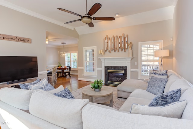 living room with wood finished floors, a ceiling fan, a high end fireplace, ornamental molding, and vaulted ceiling