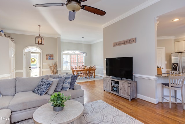 living area with ornamental molding, baseboards, light wood finished floors, and ceiling fan