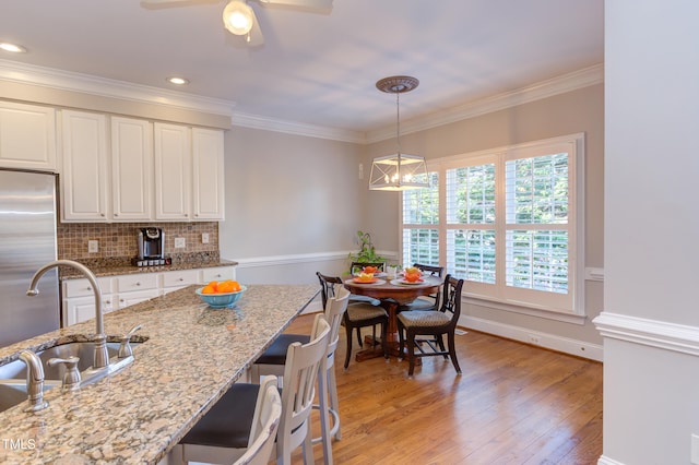 kitchen with light wood finished floors, a sink, decorative backsplash, ornamental molding, and white cabinets