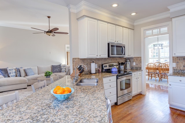 kitchen featuring light wood-style flooring, ornamental molding, a sink, appliances with stainless steel finishes, and open floor plan