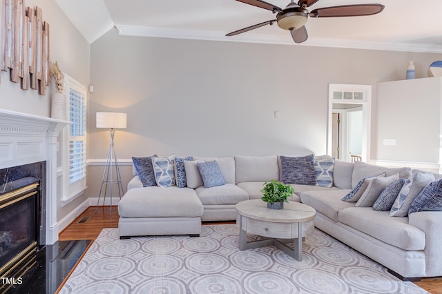 living area with a ceiling fan, wood finished floors, crown molding, a premium fireplace, and lofted ceiling