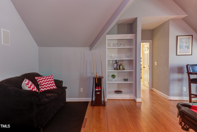 sitting room featuring built in features, lofted ceiling, baseboards, and wood finished floors