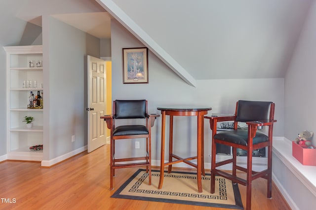 living area featuring lofted ceiling, built in features, wood finished floors, and baseboards