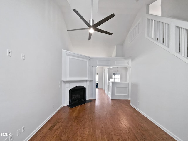 unfurnished living room featuring baseboards, ceiling fan, wood finished floors, a fireplace, and high vaulted ceiling