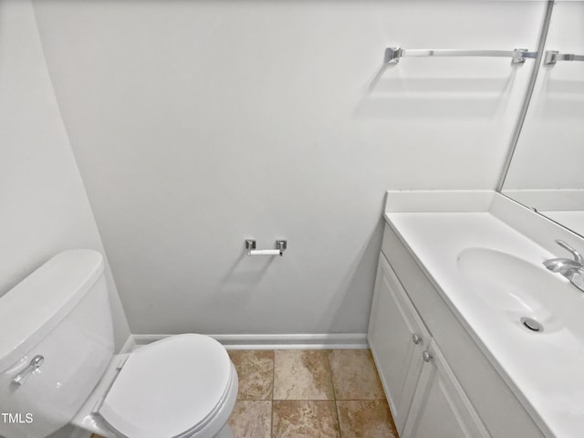 half bathroom with baseboards, vanity, and toilet