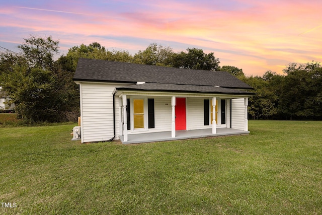 exterior space with a shingled roof, a porch, and a yard