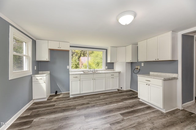 kitchen featuring dark wood-style flooring, light countertops, white cabinets, a sink, and baseboards