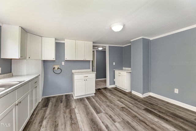 kitchen with dark wood finished floors, light countertops, white cabinets, a sink, and baseboards