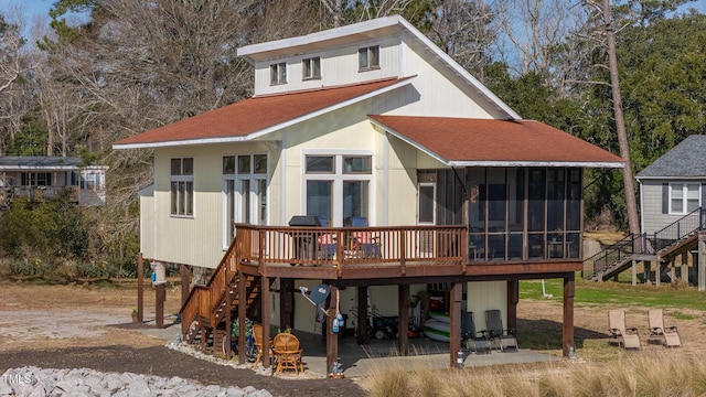 back of house with a shingled roof, a sunroom, stairway, a wooden deck, and a carport