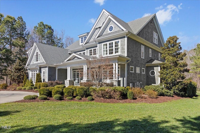 shingle-style home featuring covered porch, a front lawn, and a shingled roof