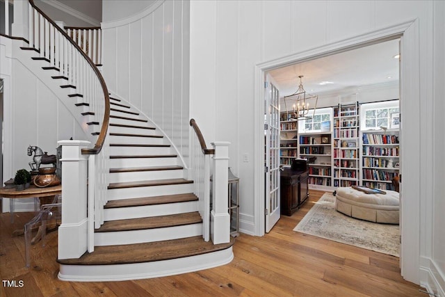 stairs with crown molding, an inviting chandelier, and wood finished floors