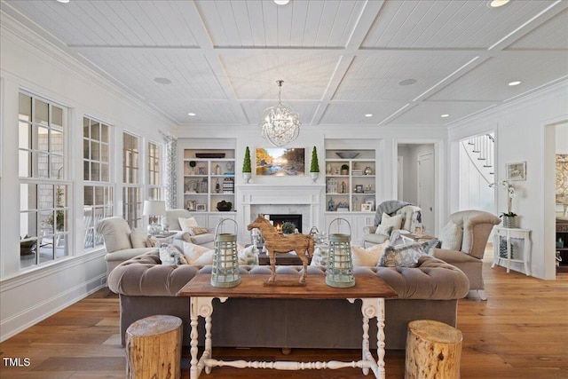 living room featuring a warm lit fireplace, built in shelves, coffered ceiling, light wood-style floors, and crown molding