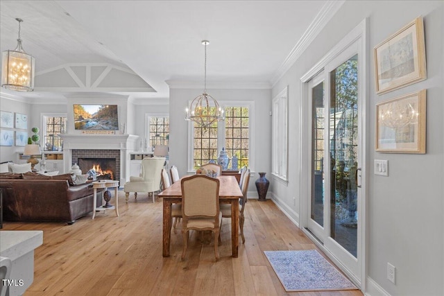 dining area featuring a chandelier, light wood-style floors, a brick fireplace, and ornamental molding