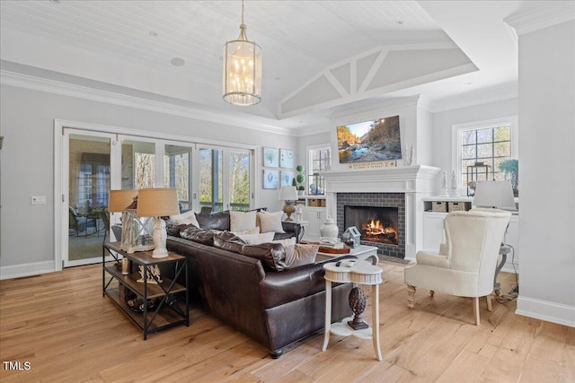 living area with crown molding, light wood finished floors, lofted ceiling, a tile fireplace, and baseboards