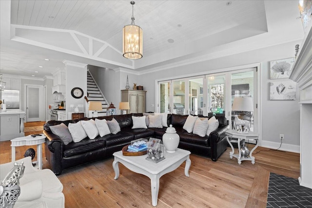 living room featuring a raised ceiling, light wood-style flooring, stairway, an inviting chandelier, and vaulted ceiling