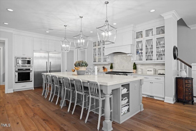 kitchen with dark wood-style flooring, white cabinets, a large island with sink, and built in appliances