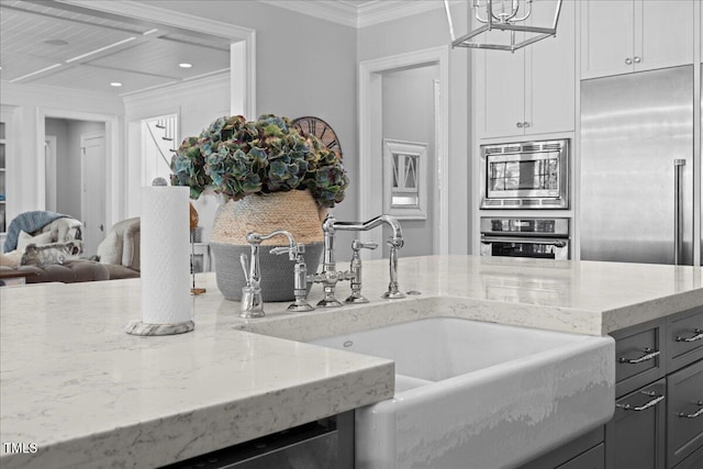 kitchen featuring built in appliances, light stone countertops, crown molding, pendant lighting, and a sink