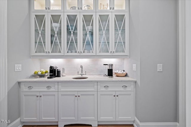 bar featuring baseboards, wet bar, a sink, and decorative backsplash