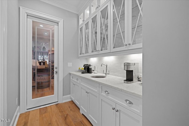 bar with a sink, baseboards, ornamental molding, light wood-type flooring, and tasteful backsplash