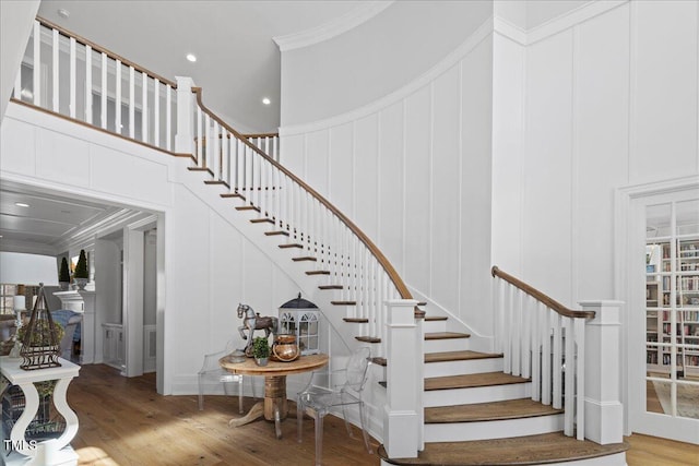 stairway with wood finished floors, a high ceiling, crown molding, a decorative wall, and recessed lighting