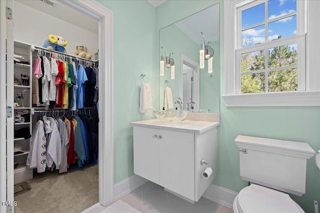 bathroom with toilet, vanity, baseboards, a spacious closet, and tile patterned floors