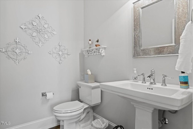 half bathroom with baseboards, a sink, and toilet