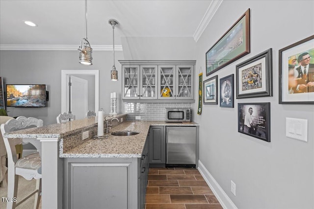 kitchen with a peninsula, stainless steel appliances, a sink, gray cabinets, and crown molding