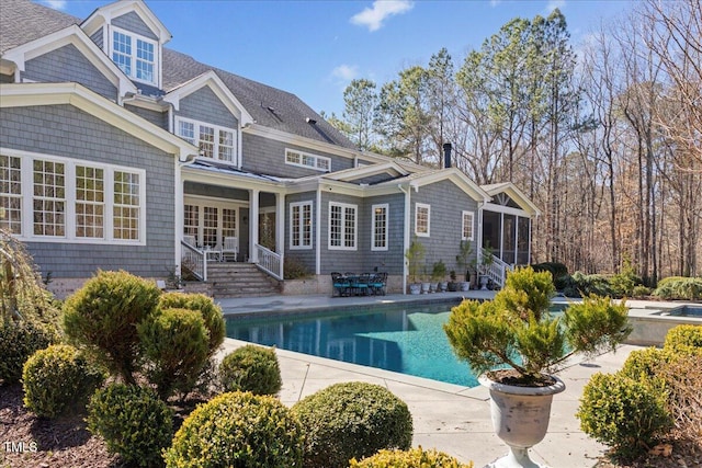 rear view of property featuring a shingled roof, a patio area, a sunroom, and an outdoor pool