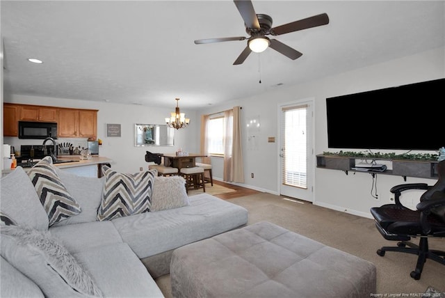 living area featuring light carpet, baseboards, and ceiling fan with notable chandelier