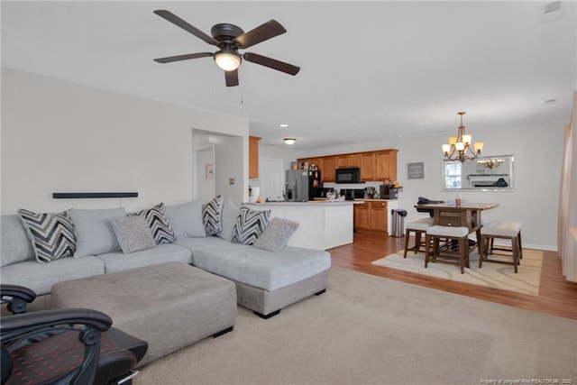 living area with ceiling fan with notable chandelier, light carpet, light wood-style flooring, and recessed lighting