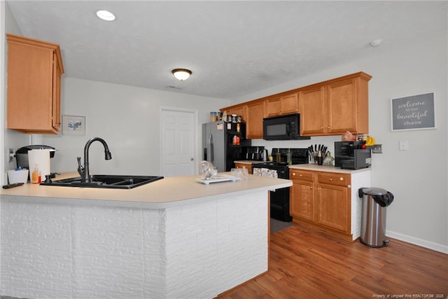 kitchen with a peninsula, a sink, light countertops, light wood-type flooring, and black appliances