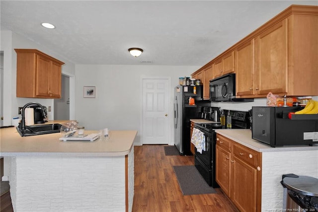 kitchen featuring brown cabinetry, dark wood-type flooring, light countertops, black appliances, and a sink