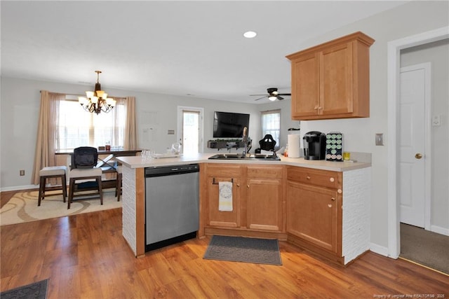 kitchen with a peninsula, a sink, light countertops, light wood-type flooring, and dishwasher