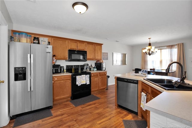 kitchen with a sink, light countertops, black appliances, brown cabinetry, and pendant lighting